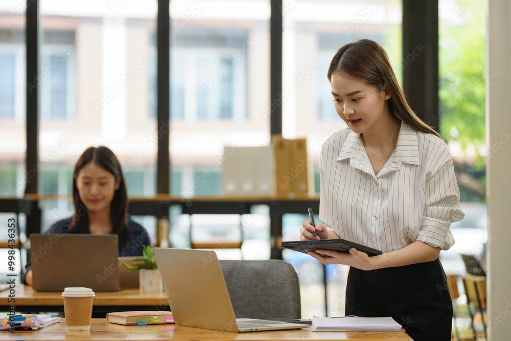 Asian businesswoman standing and holding a digital tablet while working in an office. Asian businesswoman standing and holding a digital tablet while working in an office.