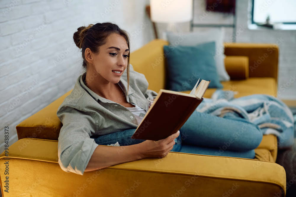 Smiling woman reading book while relaxing in living room. Smiling woman reading book while relaxing in living room.