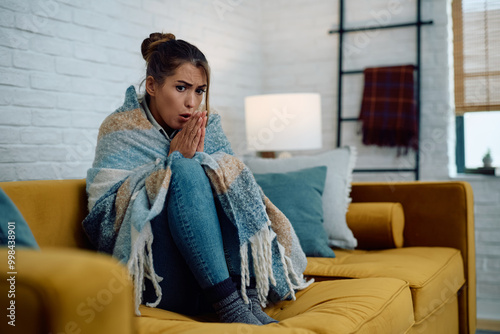 Fotografía Young woman trying to warm herself while sitting wrapped in a blanket at home with no heating