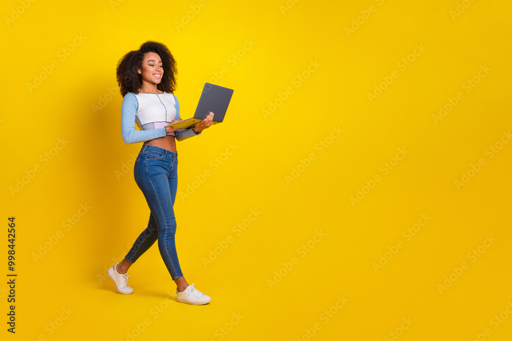 Full size photo of pretty young girl walking hold netbook wear trendy blue outfit isolated on yellow color background Full size photo of pretty young girl walking hold netbook wear trendy blue outfit isolated on yellow color background