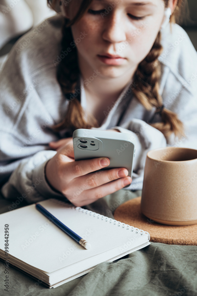 A teenage girl uses smartphone is drawing or doing homework in the bedroom. A teenage girl uses smartphone is drawing or doing homework in the bedroom.