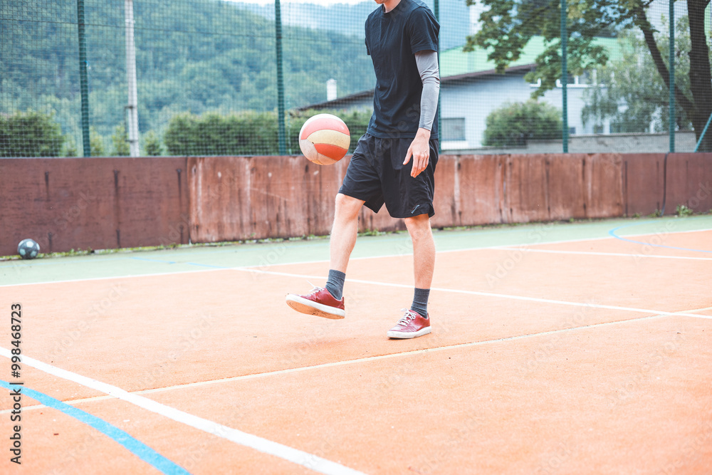 Young man dribbles a basketball on an outdoor court surrounded by nature. Dressed casually in sports attire, he showcases focus and skill during a casual practice session in a vibrant setting Young man dribbles a basketball on an outdoor court surrounded by nature. Dressed casually in sports attire, he showcases focus and skill during a casual practice session in a vibrant setting