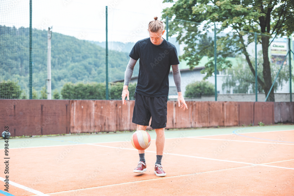 Young man casually juggles a football on an outdoor sports court, focusing on his footwork. Dressed in casual sportswear, he practices ball control in a vibrant natural setting Young man casually juggles a football on an outdoor sports court, focusing on his footwork. Dressed in casual sportswear, he practices ball control in a vibrant natural setting