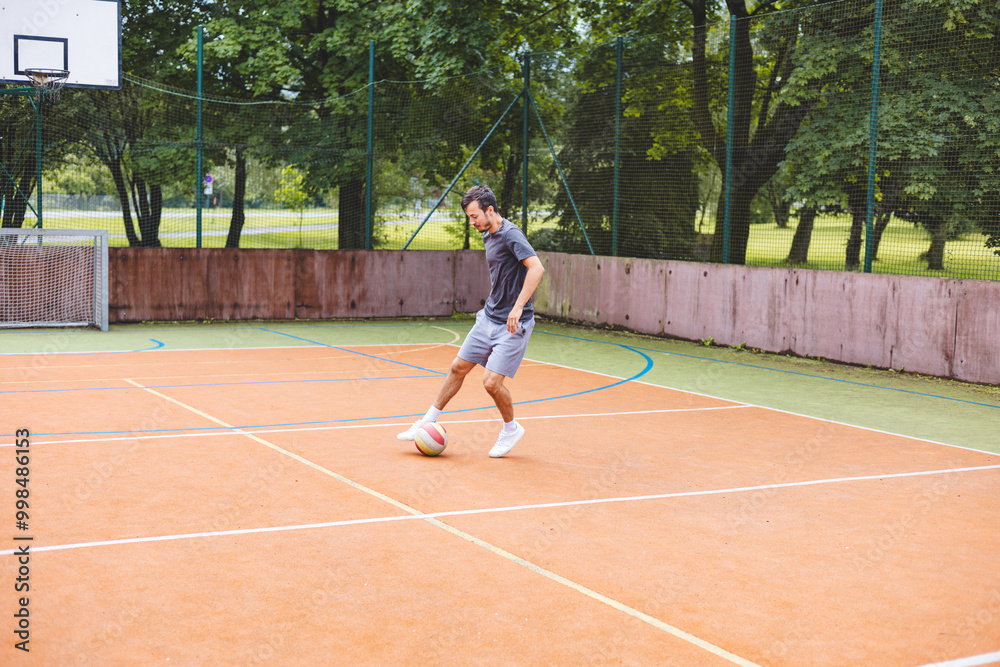 Young man dribbles a football with precision on an outdoor court, practicing his footwork in a casual environment. The court is surrounded by nature, providing a peaceful backdrop Young man dribbles a football with precision on an outdoor court, practicing his footwork in a casual environment. The court is surrounded by nature, providing a peaceful backdrop