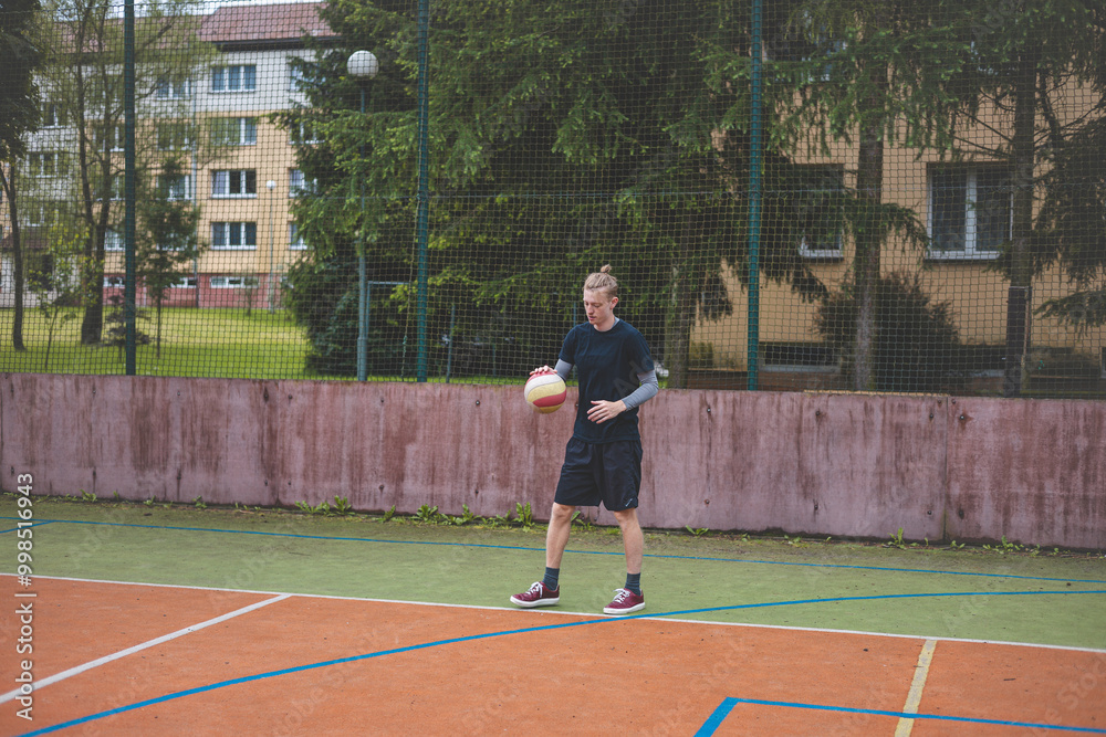 Basketball player controls and dribble the ball during a casual game on an outdoor court, bending down in focus. The court is surrounded by trees and nature, giving a peaceful and athletic atmosphere Basketball player controls and dribble the ball during a casual game on an outdoor court, bending down in focus. The court is surrounded by trees and nature, giving a peaceful and athletic atmosphere