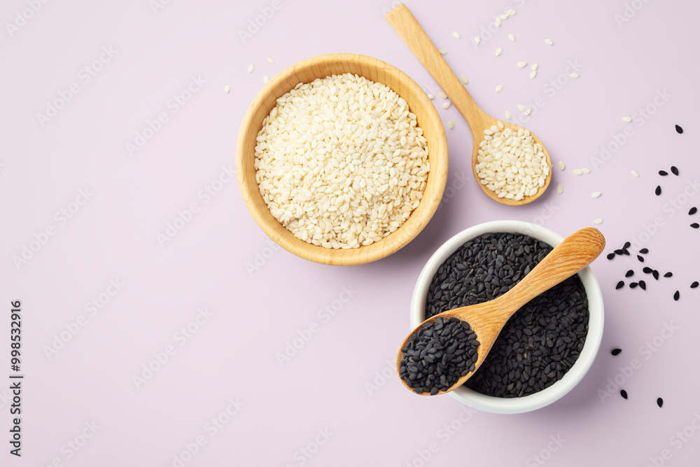 Black sesame seeds in white bowl with wood spoon and white sesame in wooden bowl isolated on pink background Black sesame seeds in white bowl with wood spoon and white sesame in wooden bowl isolated on pink background