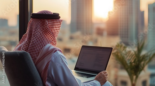 Middle Eastern man in keffiyeh using laptop for online meeting, seated and waving in a video call, back view.
