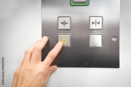 Elevator emergency call button used by passenger. Close up of woman pushing a button with a bell icon on stainless steel intercom. Call for help or stuck elevator in building. Selective focus. photo