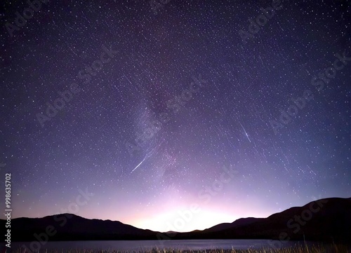 A night sky filled with stars and a shooting star streaking across it, with silhouetted mountains in the foreground photo