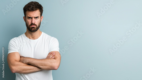 A man with furrowed brows, arms crossed tightly across his chest, conveying a sense of suspicion, standing against a pastel gray background.