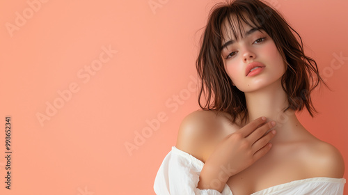 A woman gently placing her hand on her chest, her expression soft and thoughtful, standing on a pastel peach background with empty space, evoking a sense of calm and reflection.