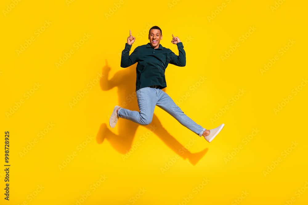 Full length photo of attractive young man jump run point up empty space dressed stylish green clothes isolated on yellow color background Full length photo of attractive young man jump run point up empty space dressed stylish green clothes isolated on yellow color background