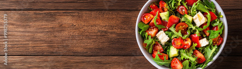 Fresh salad with vibrant greens, tomatoes, and feta cheese served in bowl on rustic wooden table, perfect for healthy meal