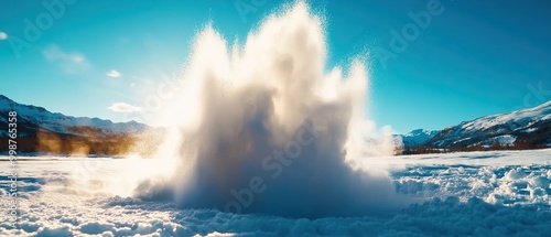 A dramatic explosion of snow and water vapor into the air, showcasing the beauty of nature under a bright blue sky in a mountainous landscape. photo