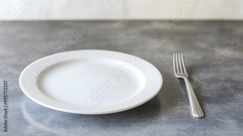 A closeup of a sleek kitchen countertop with a plain white plate and silver cutlery, emphasizing a minimal and uncluttered lifestyle. photo