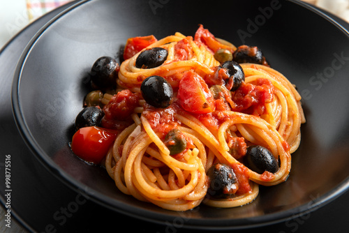 Spaghetti alla puttanesca, tradizionale ricetta di pasta condita con pomodoro, olive e capperi della cucina italiana, gastronomia europea  photo