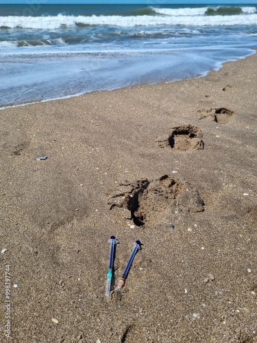 Syringes in the sand with waves in the background
