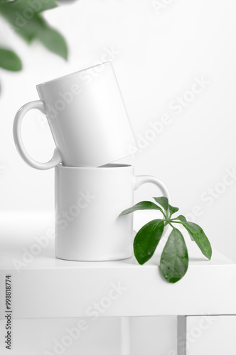 Mockup of a white tea cup or coffee mug on a white table in a Scandinavian style kitchen with a houseplant Scheffler plant. Subject template for your design, advertising with copy space