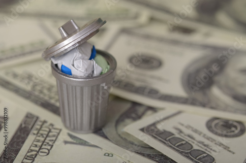 Bilde på lerret The image depicts a miniature trash can filled with crumpled paper money, symbolizing the concept of wasted money or financial loss