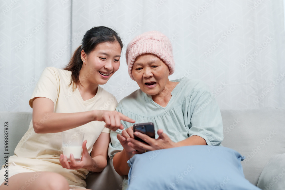bonding moment captured indoors as an elderly mother and daughter interact with technology. The warmth and intimacy are evident as the sea green-clad woman focuses on mobile phone. bonding moment captured indoors as an elderly mother and daughter interact with technology. The warmth and intimacy are evident as the sea green-clad woman focuses on mobile phone.
