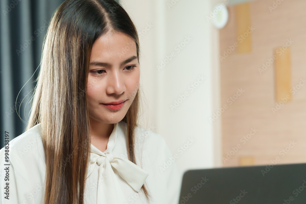 Asian woman working from home sitting at desk wearing white blouse focused on laptop relaxed home office environment modern workspace professional lifestyle indoors. Asian woman working from home sitting at desk wearing white blouse focused on laptop relaxed home office environment modern workspace professional lifestyle indoors.