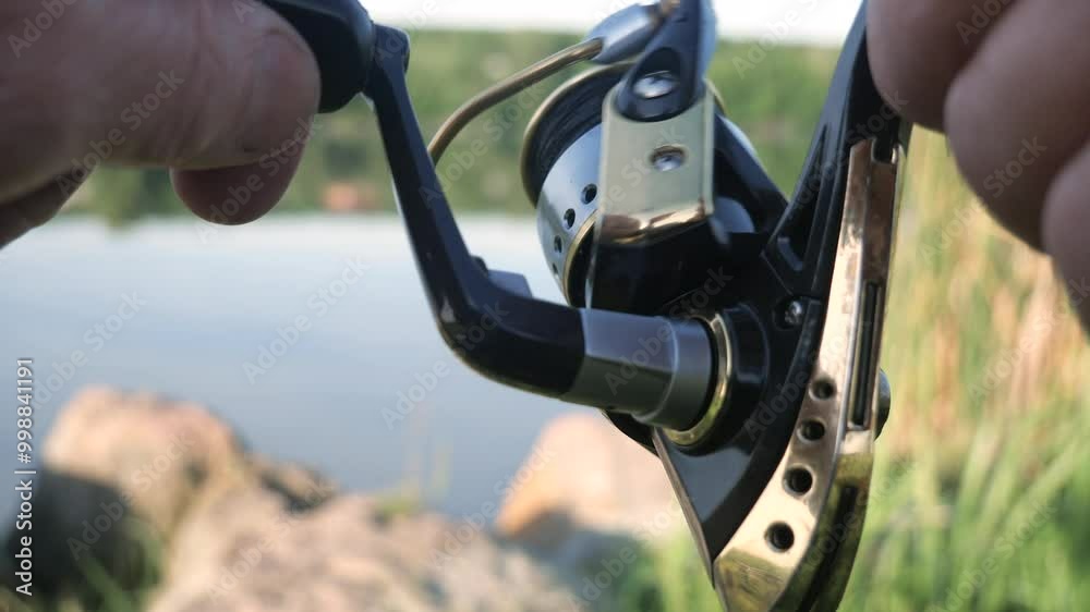 A fisherman's hand slowly spins a spinning reel during sport fishing, in the summer outdoors, on a river. Slow motion. A fisherman's hand slowly spins a spinning reel during sport fishing, in the summer outdoors, on a river. Slow motion.