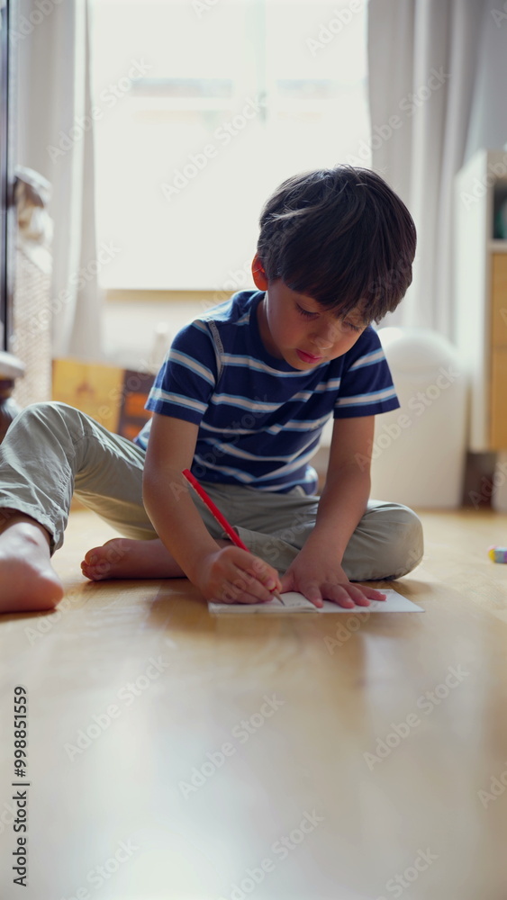 Young boy intently drawing on paper while sitting on the floor, focused on his creative activity in a bright and inviting room, nurturing artistic skills Young boy intently drawing on paper while sitting on the floor, focused on his creative activity in a bright and inviting room, nurturing artistic skills