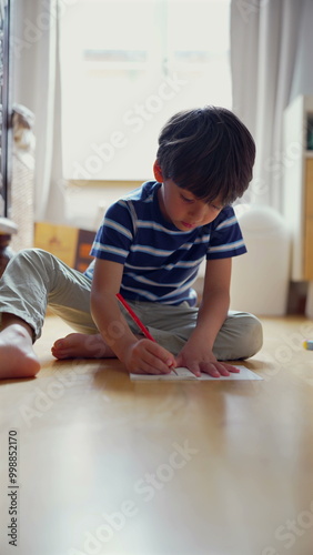 Young boy intently drawing on paper while sitting on the floor, focused on his creative activity in a bright and inviting room, nurturing artistic skills