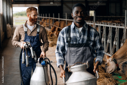 Farm business, industry of eco dairy factory. Two workers with jug of milk and milking machine at cowhed photo