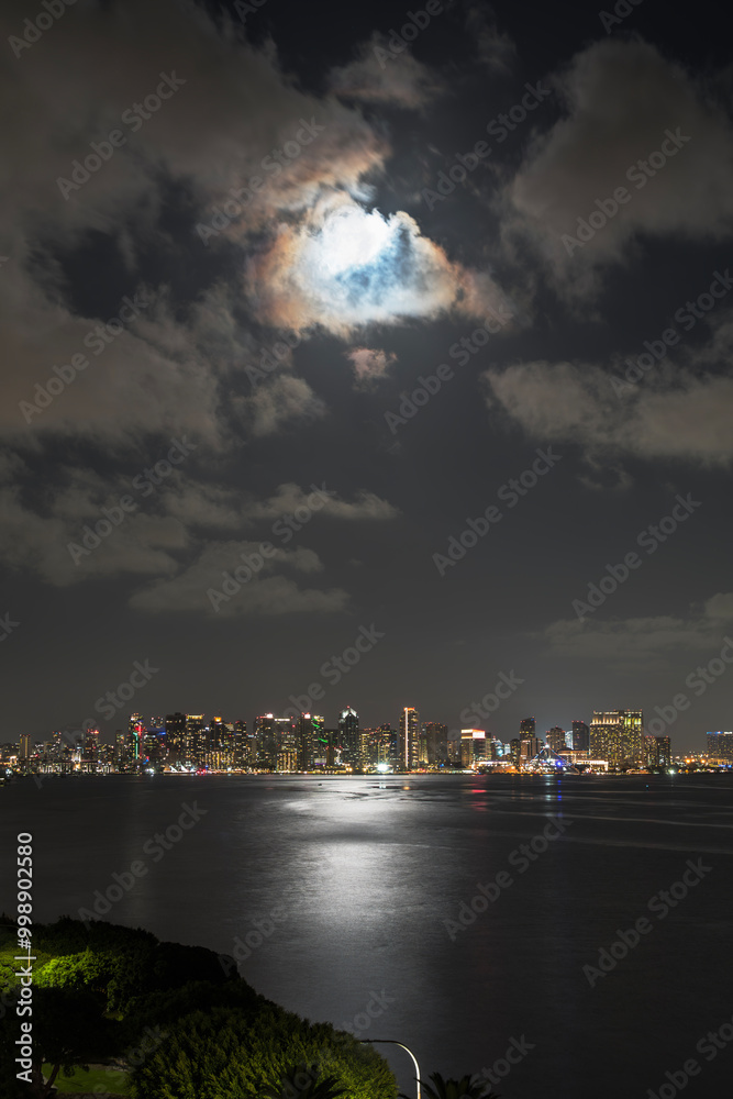 Fototapeta premium Moonlight reflecting on San Diego bay with city skyline in background. Vertical view.