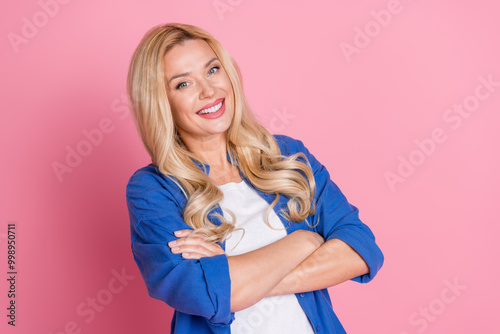 Portrait of toothy beaming pretty woman with wavy hairstyle dressed blue shirt holding arms folded isolated on pink color background