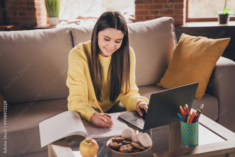 Photo of charming teen girl sit sofa do homework online wear yellow clothes modern interior flat indoors Photo of charming teen girl sit sofa do homework online wear yellow clothes modern interior flat indoors