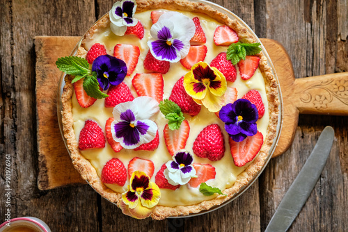 Almond tart with custard cream and strawberries decorated with edible flowers photo