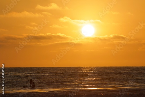 Surfer sitting on surfboard in ocean silhouette during golden hour sunset in Pacific beach, San Diego, California photo