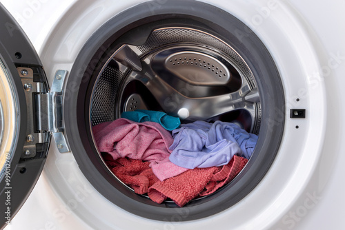 Colourful load of clothes and towels in a washing machine drum with open door photo