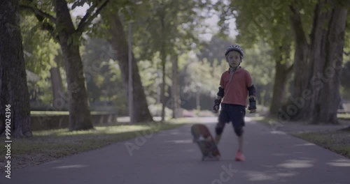 Wallpaper Mural Young boy standing on the pathway in a park wearing protective gear and holding a skateboard upright, looking into the distance with trees surrounding the area Torontodigital.ca