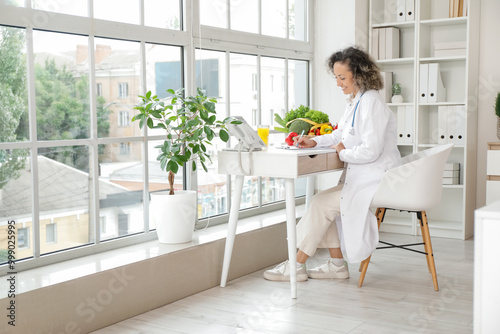 Mature female nutritionist writing on clipboard at table in office