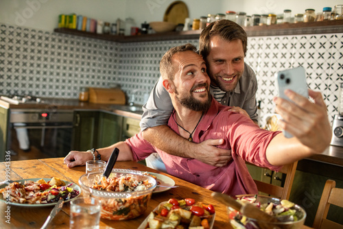 Gay couple enjoying lunch together at home and taking selfie