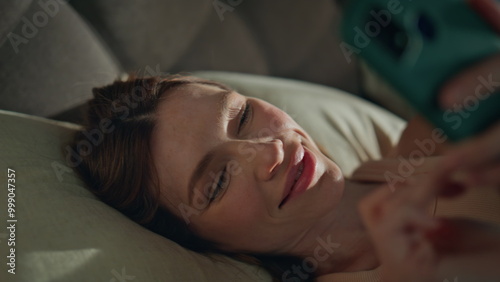 Girl smartphone lying bed pillows waking up early morning close up. Sleepy woman