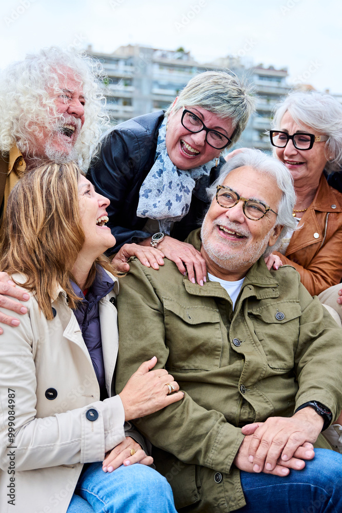 Fototapeta premium Vertical. Group of seniors grey hair joyful people having fun together sitting on bench in urban. Cheerful mature Caucasian friends meeting talking funny enjoying free time laughing autumn day outdoor