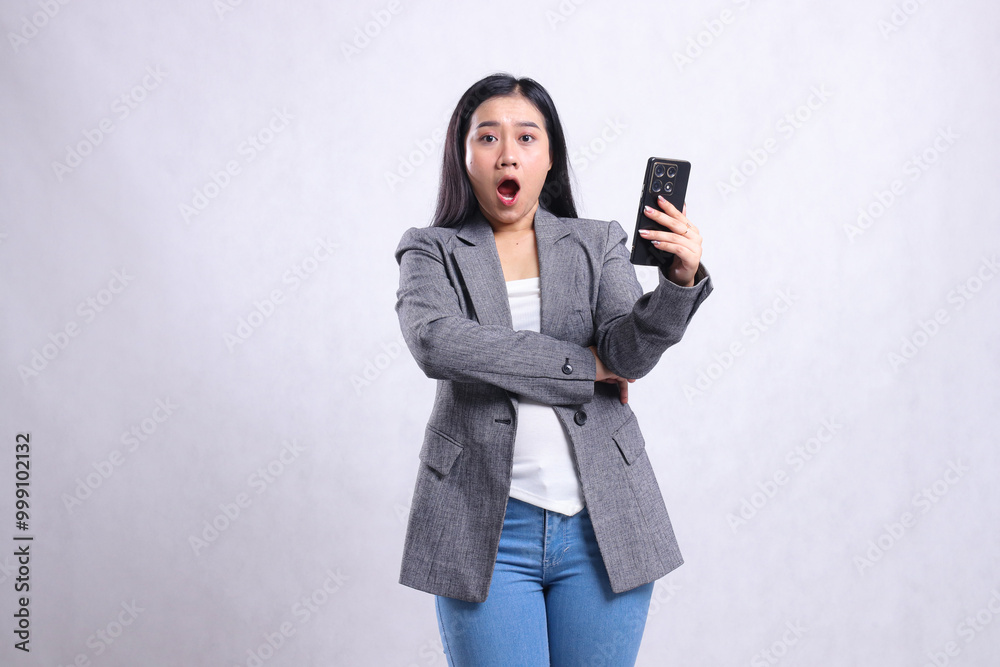 portrait of beautiful young office woman surprised to camera holding cellphone wearing grey suit isolated on white background. for technology, lifestyle, shopping, transaction content portrait of beautiful young office woman surprised to camera holding cellphone wearing grey suit isolated on white background. for technology, lifestyle, shopping, transaction content
