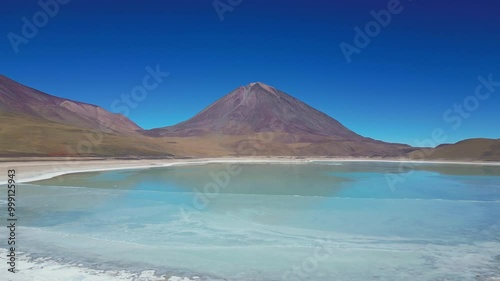Drone shot Flying over partially frozen blue salt lake (Laguna Verde) in the Bolivian Andes towards the inactive volcano Licancabur