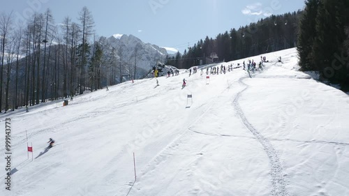Skiers descend a steep, pristine snowy hill with visible ski tracks and racing gates. A thrilling scene for ski racing or winter sports.