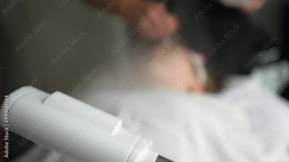 Facial steam machine operating during a skincare treatment, with an aesthetician applying a product in the blurred background. The focus on the machine highlights its role in beauty and spa treatments