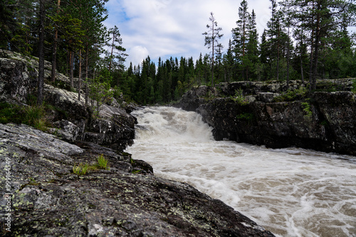 Sognstupet Waterfall cascades dramatically over rocky terrain, surrounded by lush trees in Idre, nature's raw power and beauty along the Storån River in the forest wilderness of Dalarna Sweden. photo