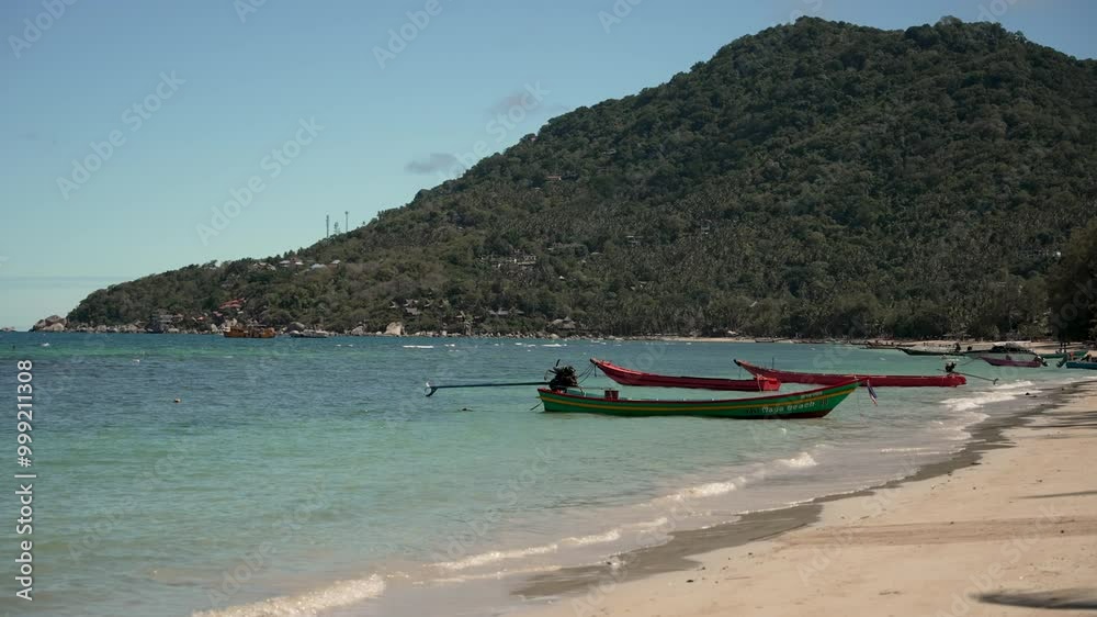 Serene view of moored wooden longboats beside a tropical beach with clear waters and lush hills in Thailand. slow motion shot Serene view of moored wooden longboats beside a tropical beach with clear waters and lush hills in Thailand. slow motion shot
