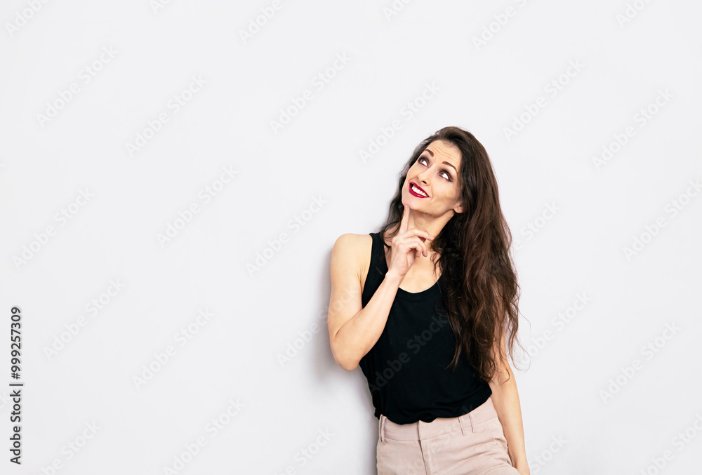 Beautiful positive fun makeup woman in black casual top looking up with finger under the face on empty isolated copy space studio background. Closeup Beautiful positive fun makeup woman in black casual top looking up with finger under the face on empty isolated copy space studio background. Closeup