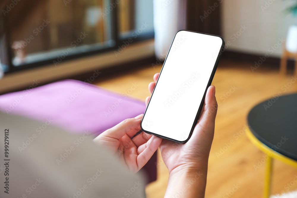 Mockup image of a woman holding mobile phone with blank desktop white screen at home