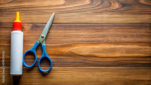 A pair of scissors and a glue stick positioned to the right on a wooden desk, with extra space on the left for design or text overlay.