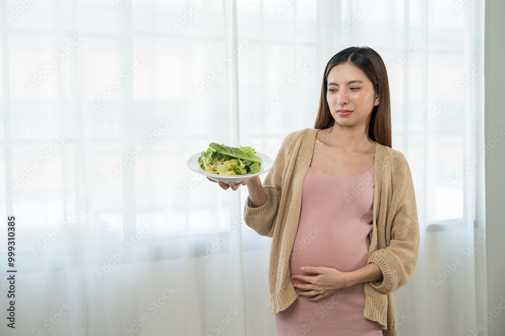 Unhappy young asian pregnant woman feeling with morning sickness to vegetable salad, frustrated young lady refusing eating vegetable, concept of hate vegetarian nutrition Unhappy young asian pregnant woman feeling with morning sickness to vegetable salad, frustrated young lady refusing eating vegetable, concept of hate vegetarian nutrition